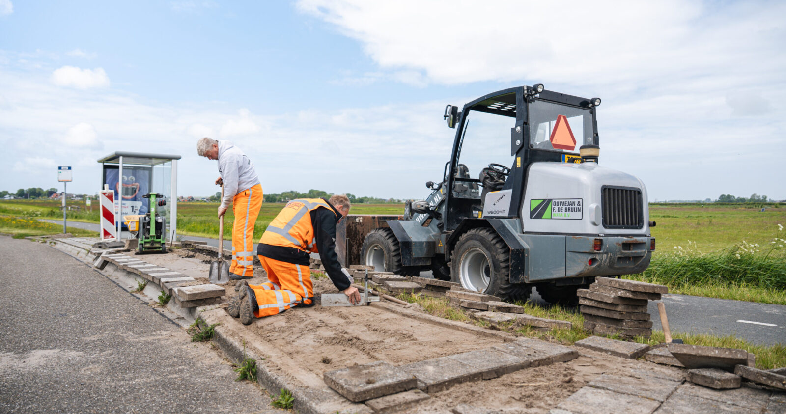 Vincent en Rob voeren bestratingswerkzaamheden uit bij een bushalte.