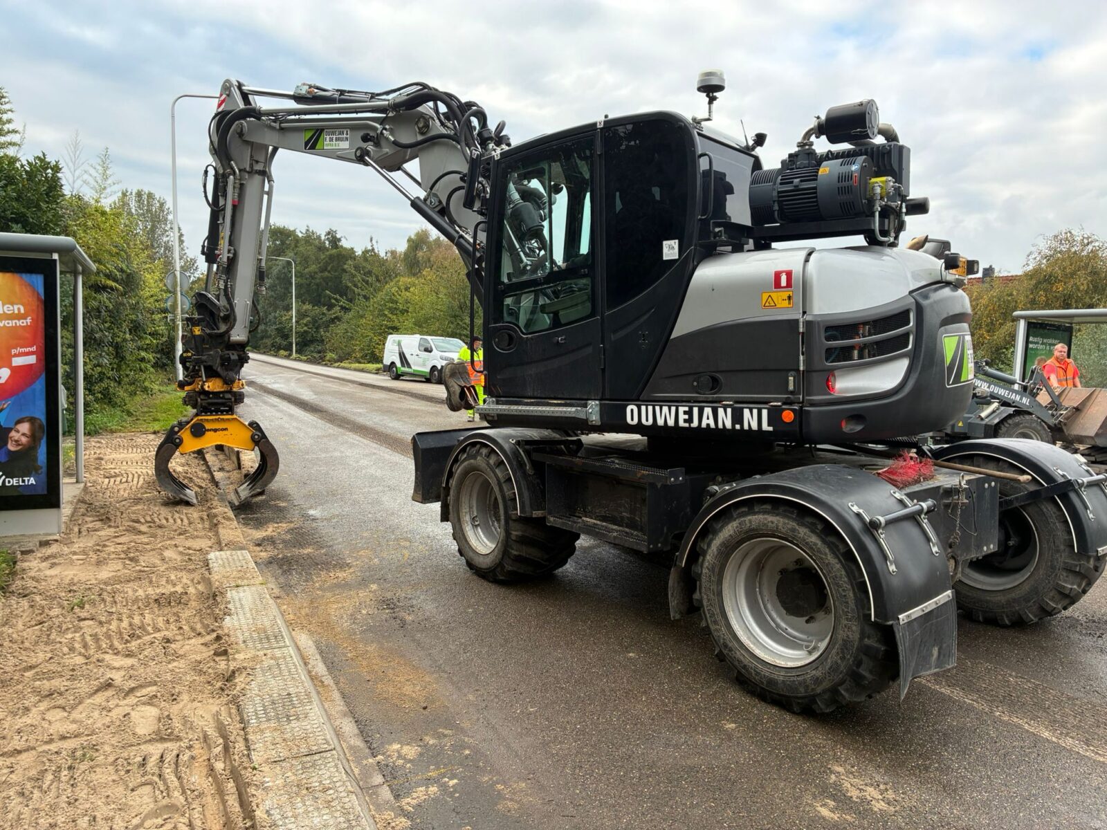 Mobiele graafmachine met grijper voert werkzaamheden uit langs de weg tijdens een infrastructuurproject van Ouwejan.