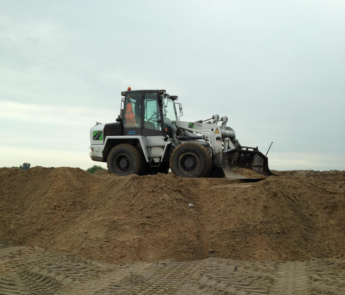 Shovelmachinist bestuurt een shovel met zeefbak tijdens grondwerk op een zanddepot.